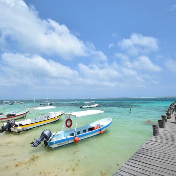 small boats anchored on the beach as people stroll up and down the pier