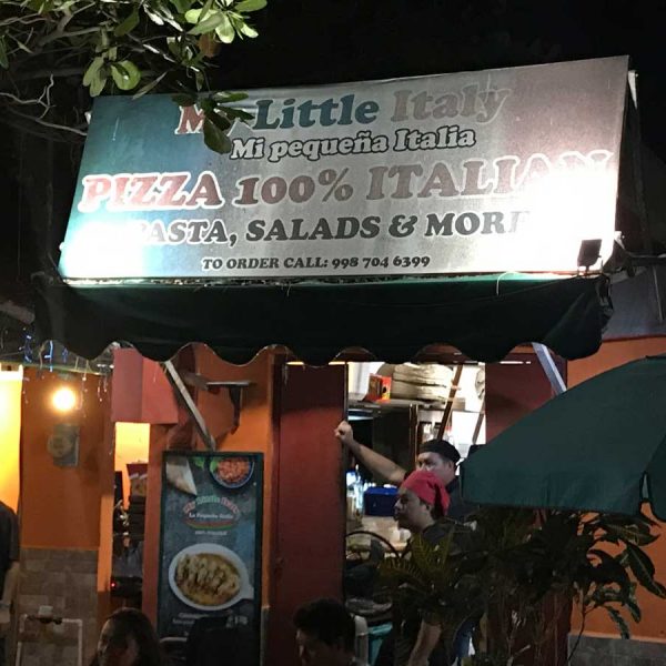diners enjoy their pizza seated at tables outdoors. A sign reads pasta, salads & more