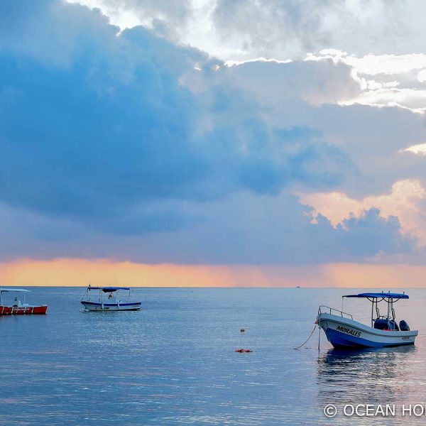 small boats anchor just offshore amidst a golden sunset