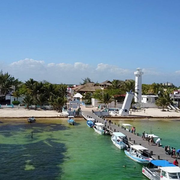 A dock stretches out onto the emerald ocean aside the leaning lighthouse of puerto morelos