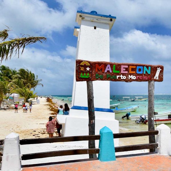 Vacationers pose for pictures by the leaning lighthouse on the beach of puerto morelos